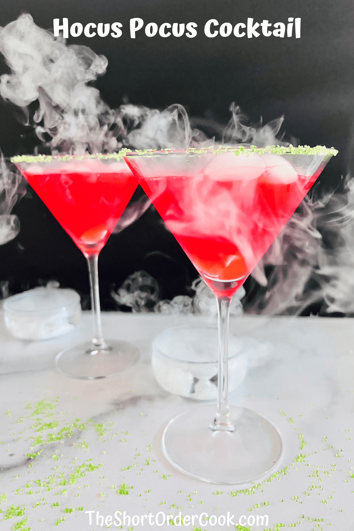 Two martini glasses filled with red hocus pocus cocktail with smoke coming from each.