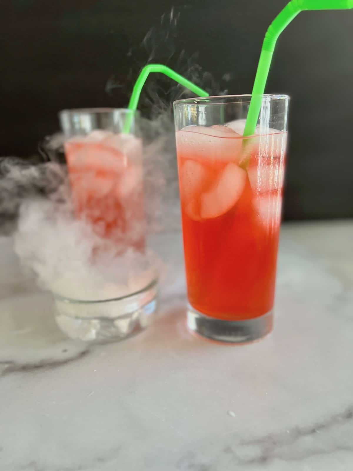 A small dish with dry ice starting to fog up like smoke next to drinks.