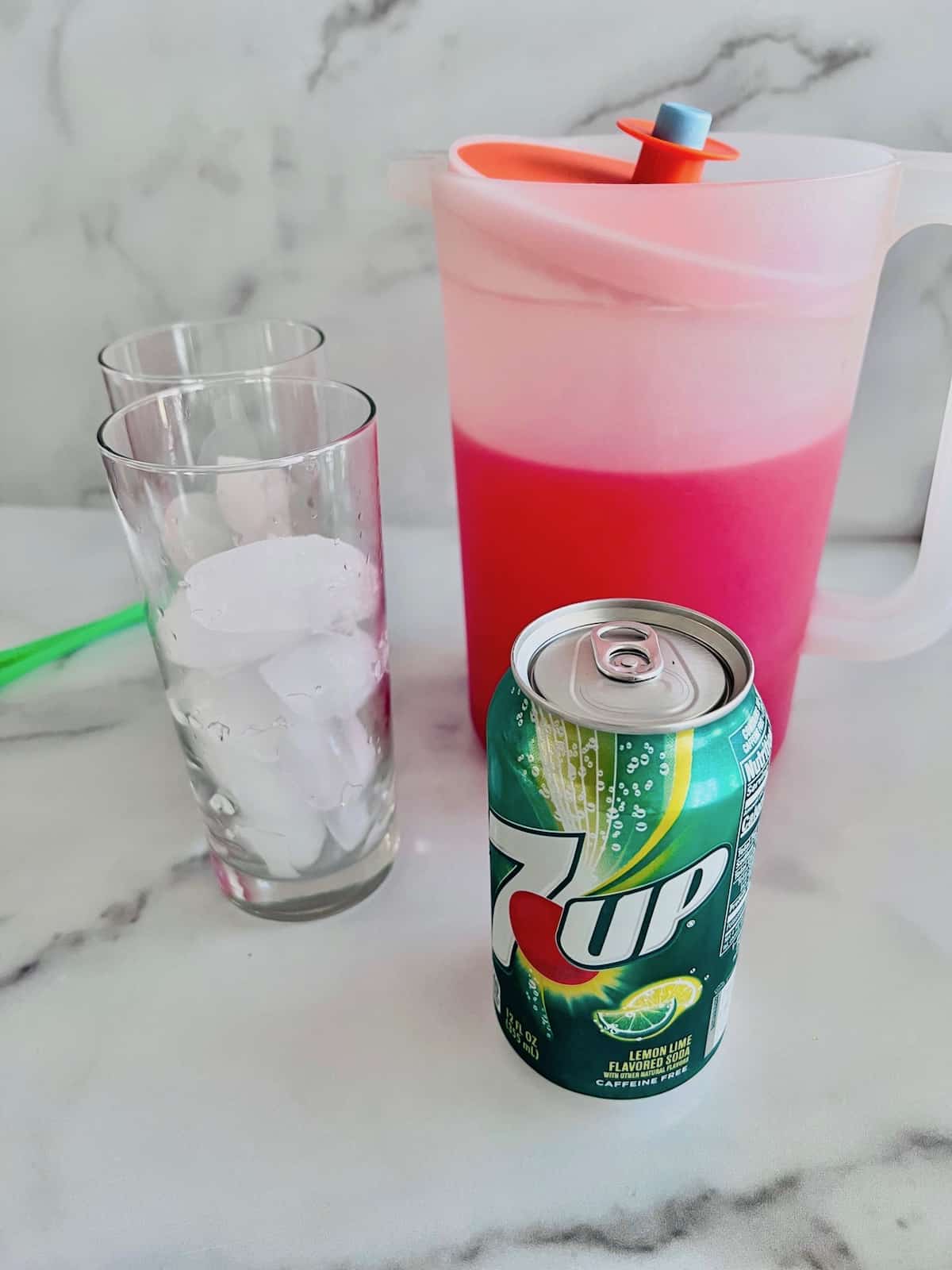 Glasses filled with ice and next to pitcher of punch and a can of 7up.