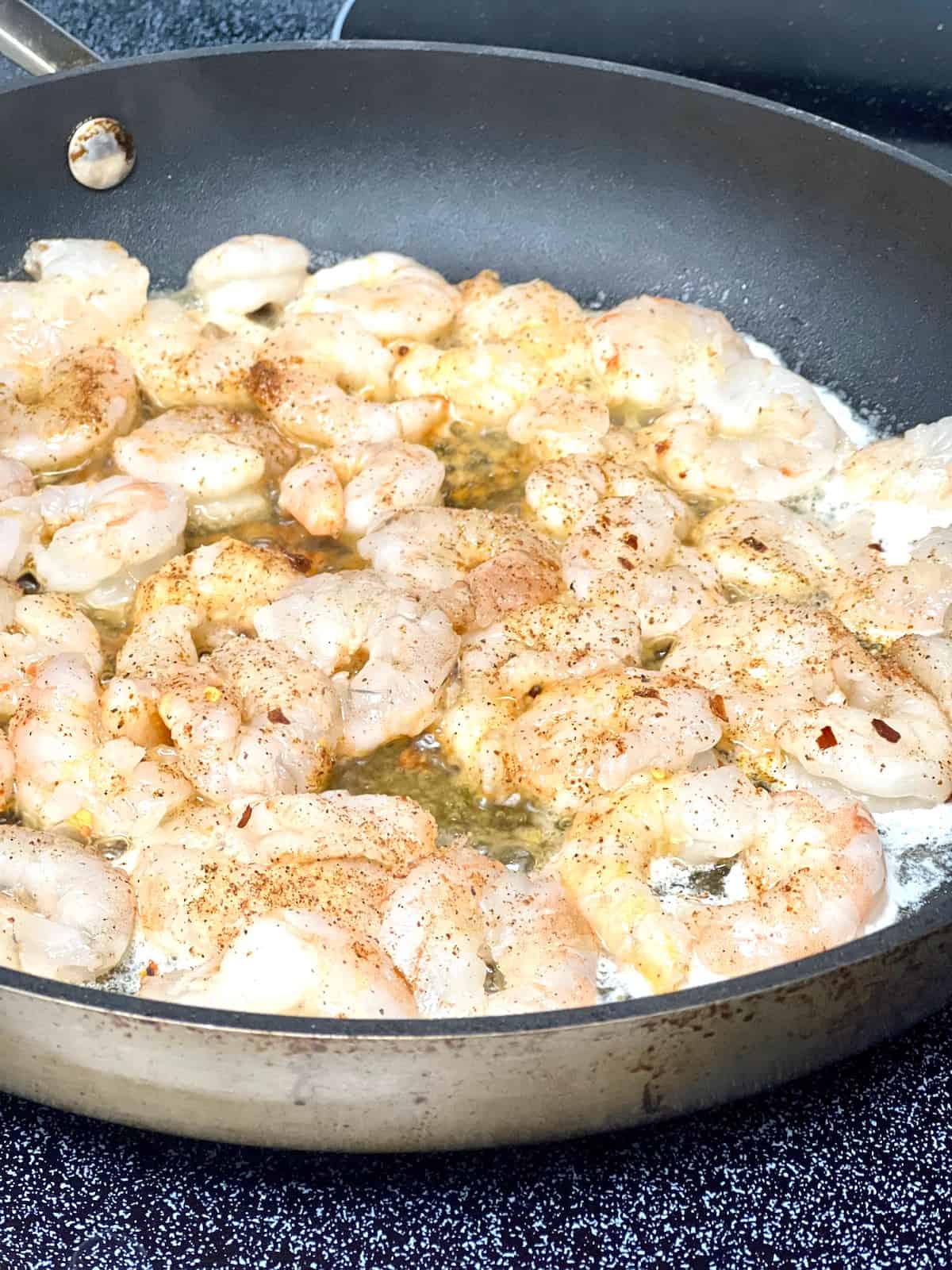 Pan filled with raw shrimp sizzling in butter.