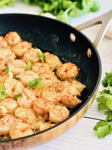 Skillet filled with pan-seared shrimp topped with parsley.