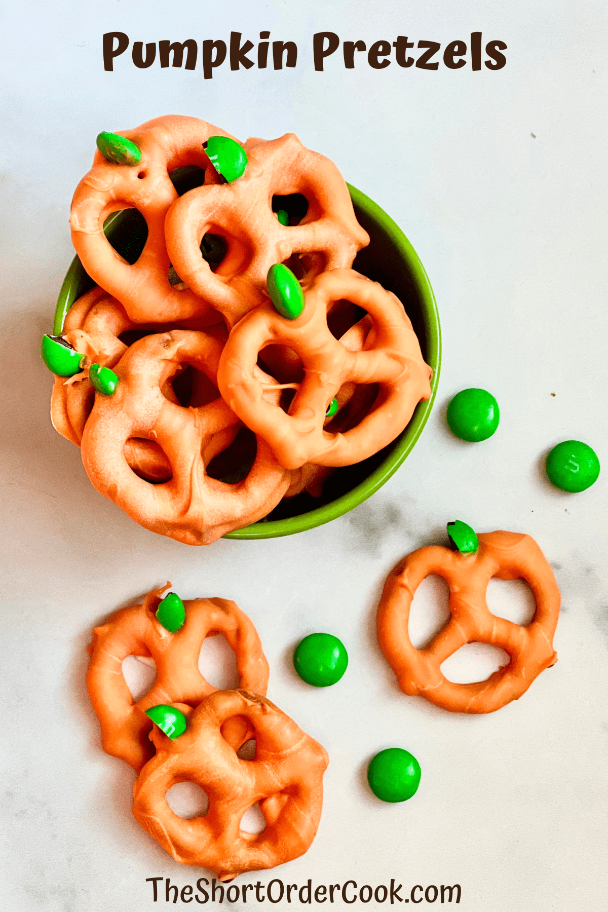 A bowl of pretzels with orange candy coating that are pumpkin-shaped in a bowl and on a table.