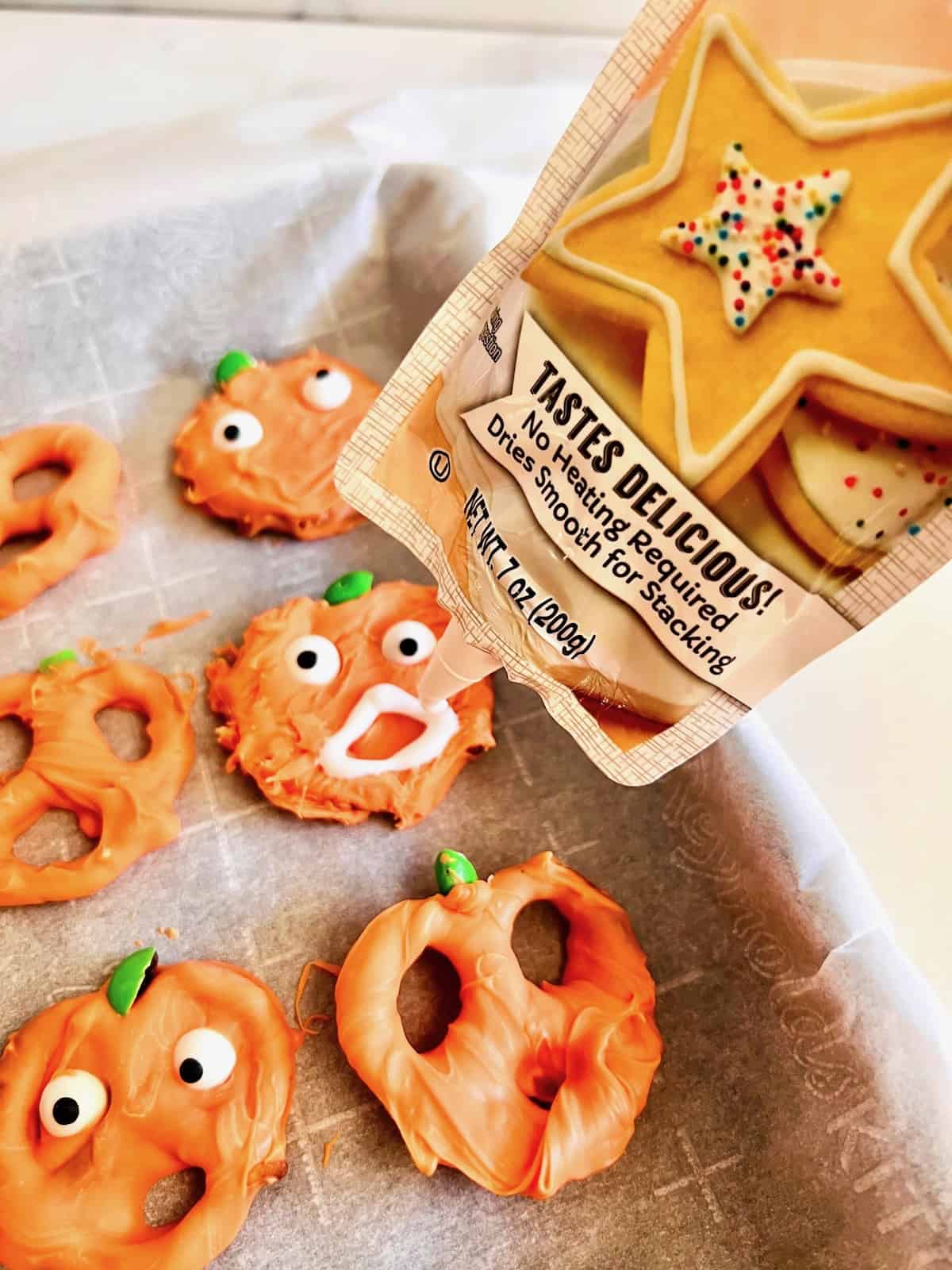 Using Cookie Icing to add Jack o Lantern faces onto orange pumpkin pretzels.