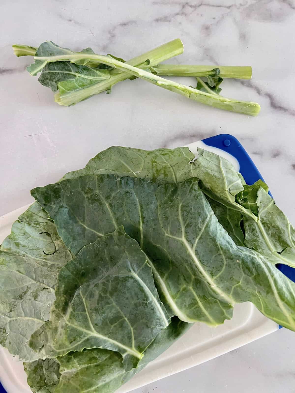 Collard leaves on a cutting board and the removed stems in a pile to the side.
