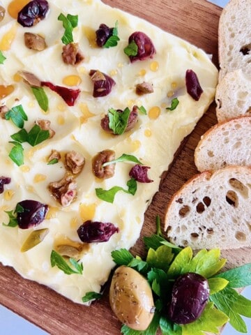 Butter board topped with olives and honey with sliced baguette.