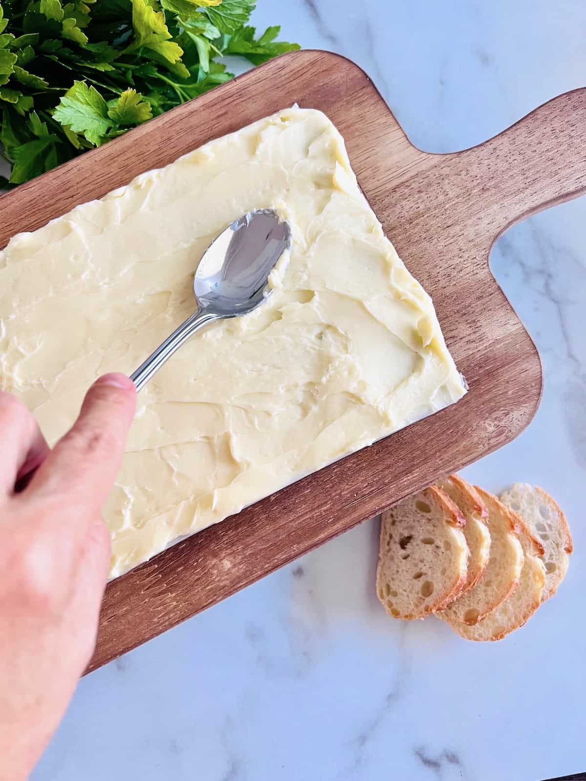 Using back of spoon to spread out soft butter on wooden board.