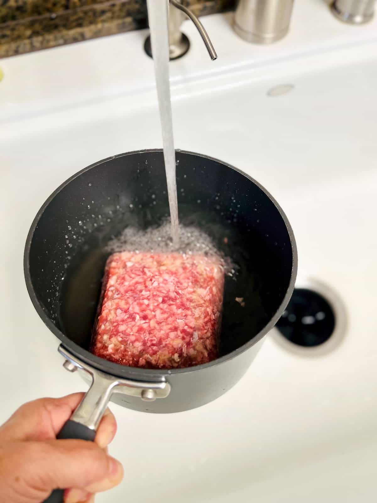 Adding water to a pot with ground beef in it.