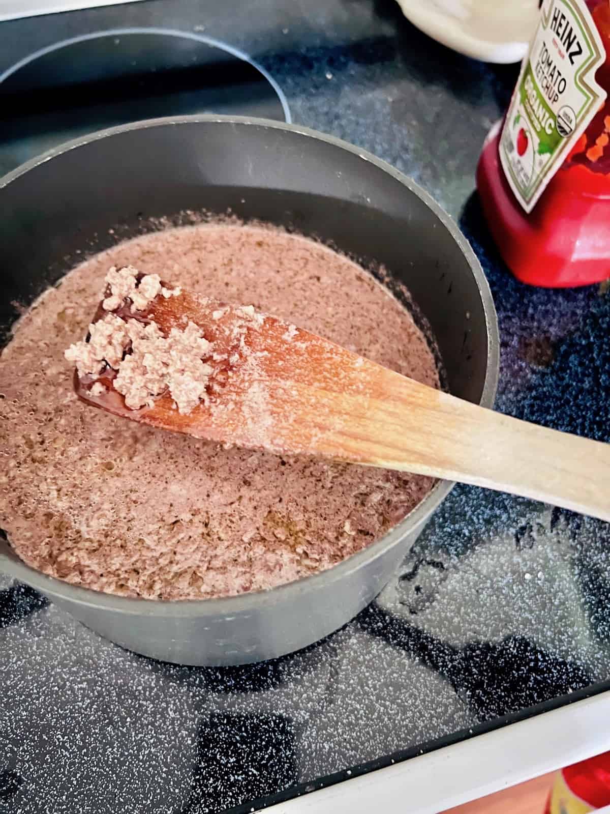 Ground beef done boiling in a pot with fine pieces on a wooden spoon.