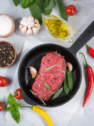 Best Pans for Searing Steaks Pan with ingredients aroudn it and a steak in the pan ready to cook.