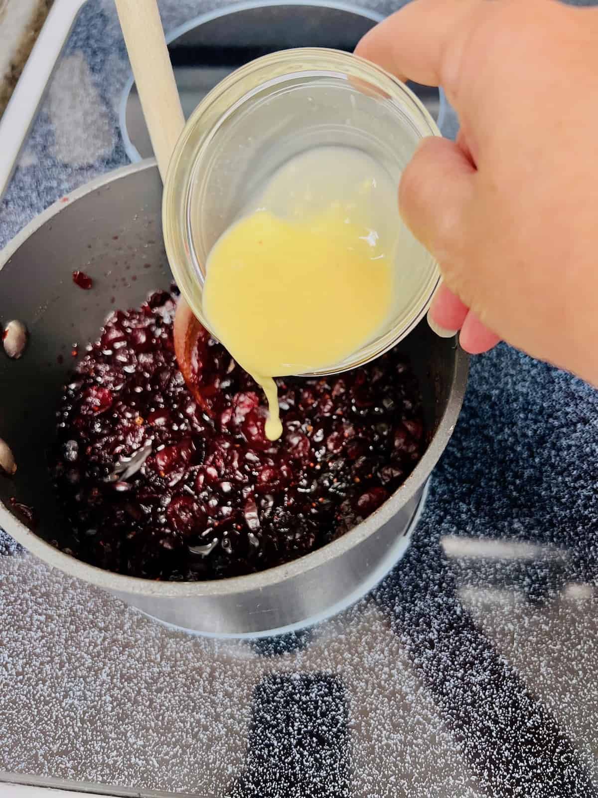 Pouring the cornstarch slurry into the cooked dried cranberries to thicken the sauce.