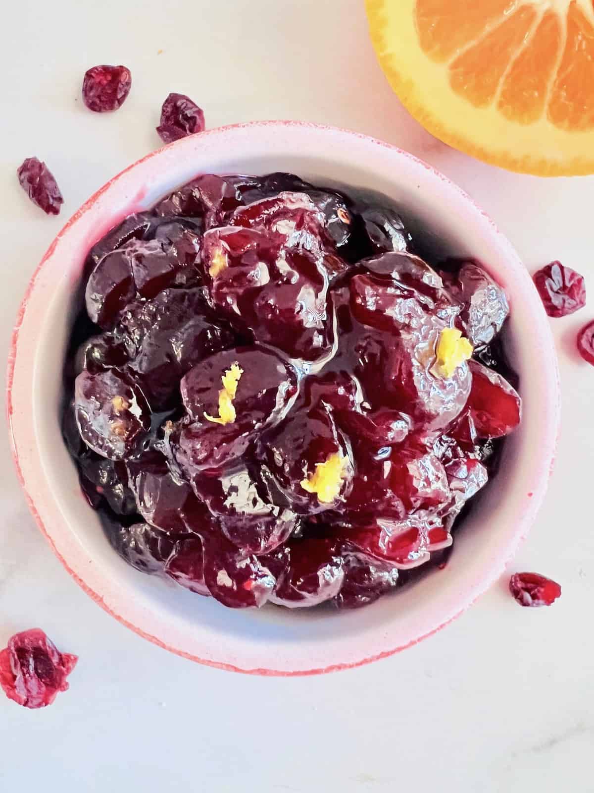 Cranberry Sauce from Dried Cranberries in a red bowl topped with fresh orange zest.