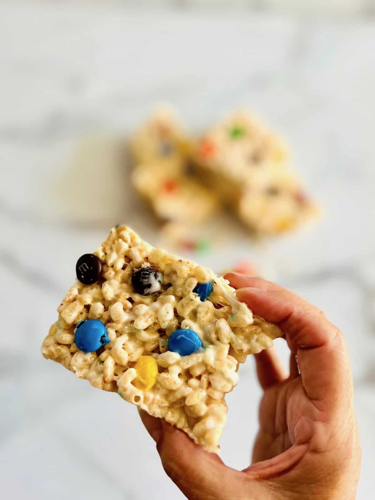 M&M Rice Krispies Treats Handing holding a square up ready to eat.