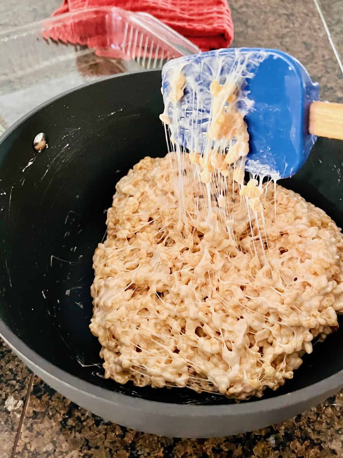 Rice krispies added to melted marshmallow and stretching from the pot to the spatula.