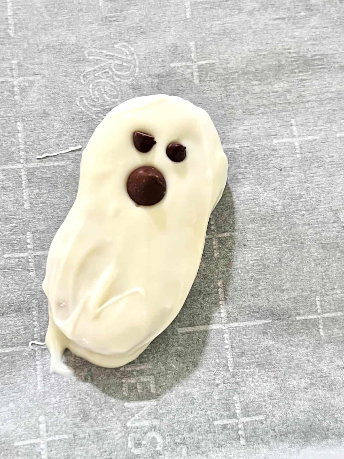 Nutter Butter decorated like a white ghosts with chcoolate chip eyes and mouth on parchment.