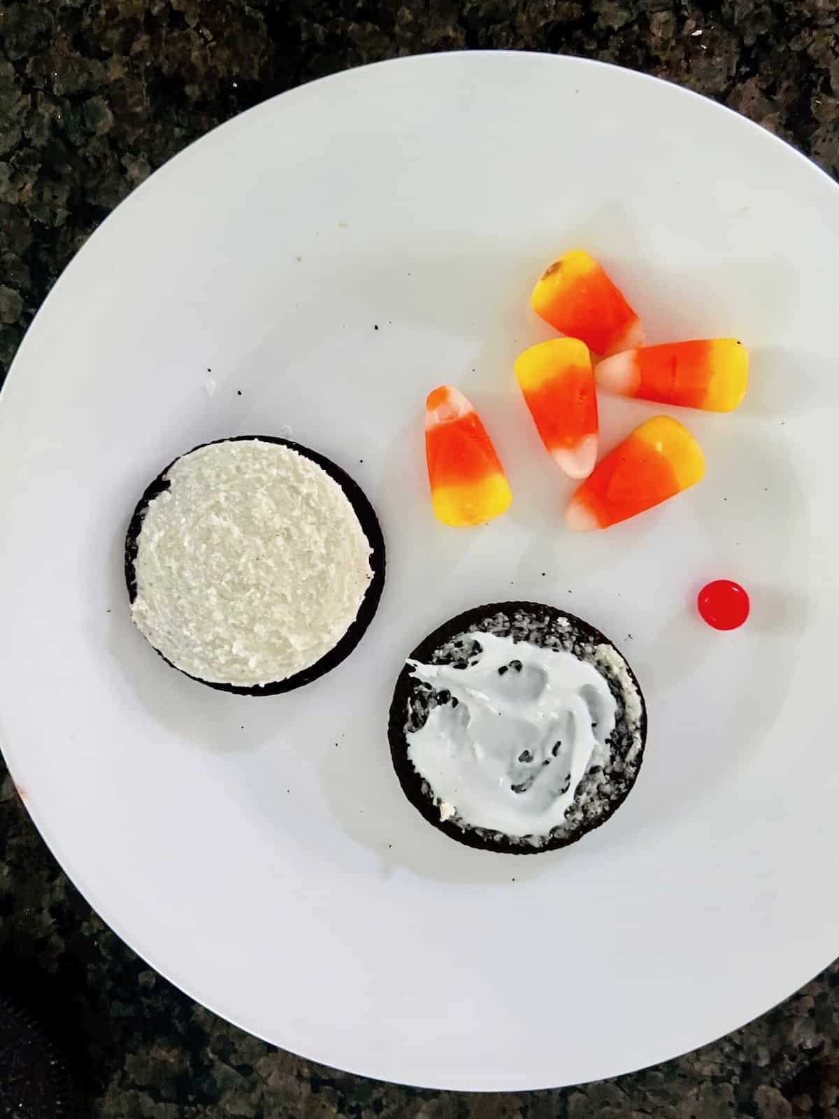 Opened Oreo on a plate with frosting candy corns and a red hot.