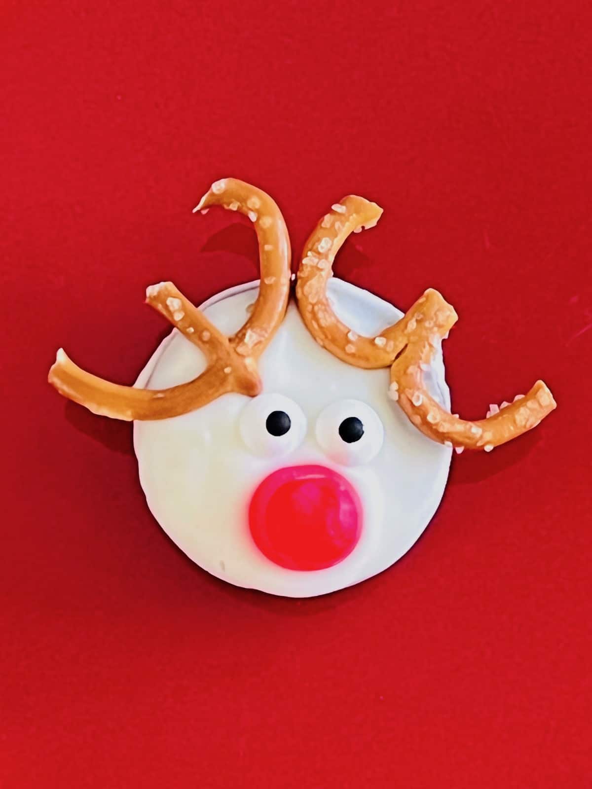 An Oreo cookie in white candy decorated like Rudolph the reindeer.