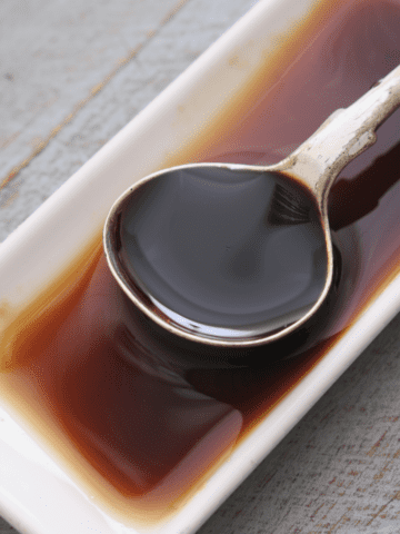 A shallow white dish with homemade Worcestershire sauce and a spoon.