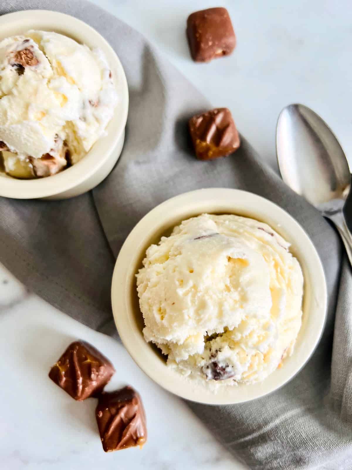 Candy Bar Ice Cream Overhead two scoops in bowls with spoon and unwrapped candies.