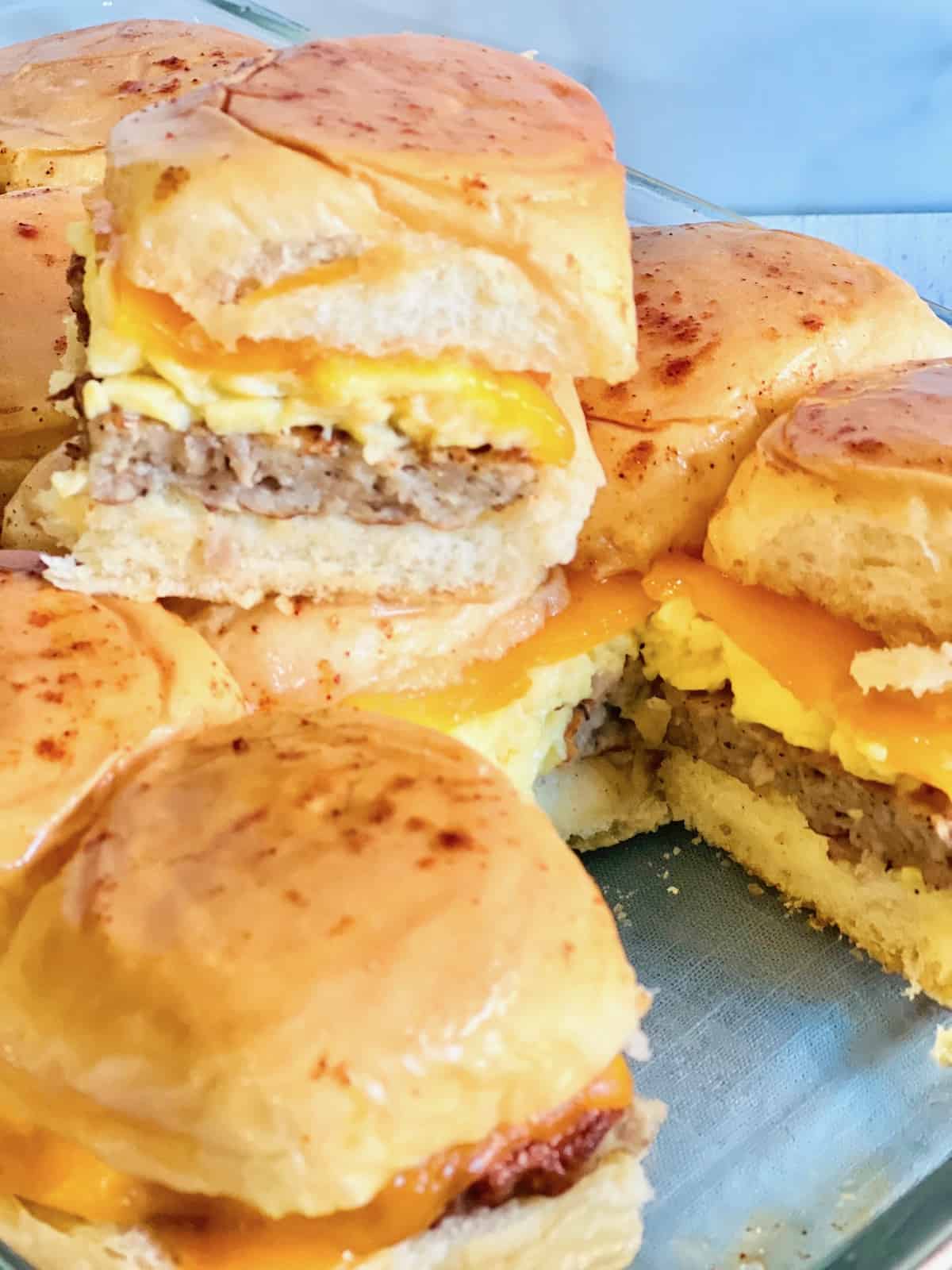 Sliders In a baking dish with one taken out and placed on top exposing the cheese egg and sausage layers.