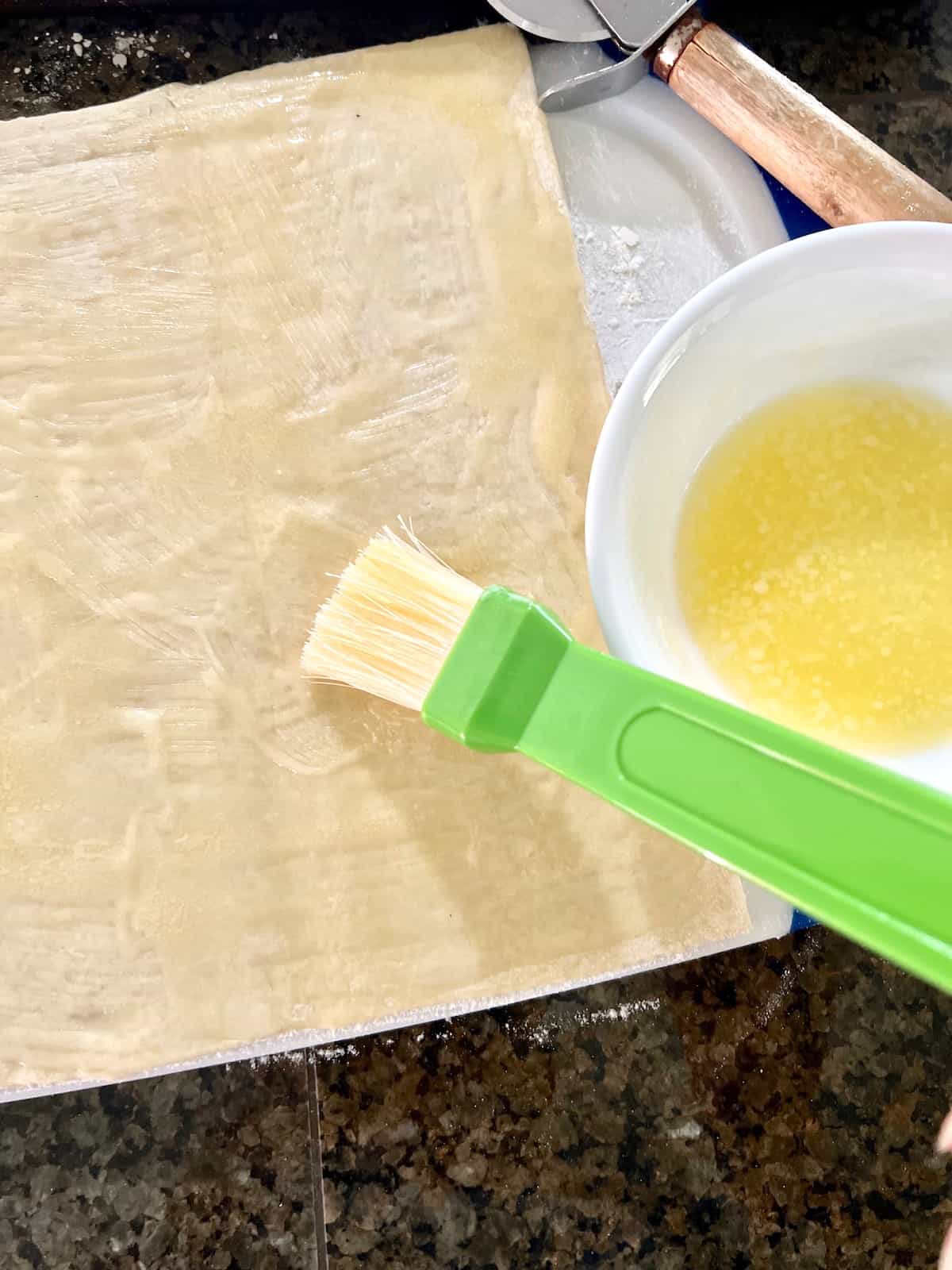Brushing melted butter on the puff pastry.