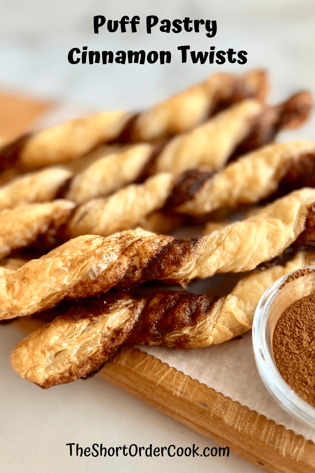 Cinnamon twists of puff pastry on a cutting board with a bowl of cinnamon.