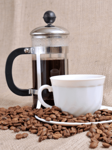 Best Coffee Grinders for French Press French press and a cup of coffee with beans on the table.