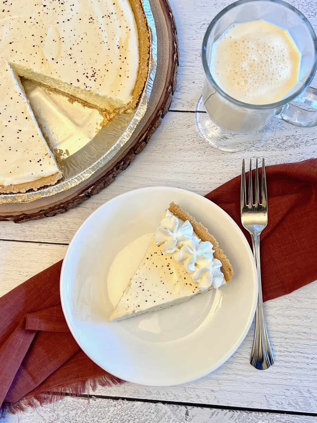 No-Bake Eggnog Pie Overhead of full eggnog pie with slice cut out and on a plate plus glass of eggnog.