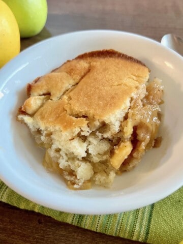 Gluten-free Apple Cobbler in a bowl with spoon and whole apples next to it.