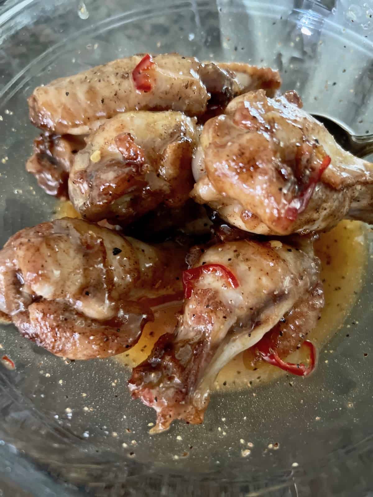 Wings in a bowl covered with hot honey lemon pepper sauce.