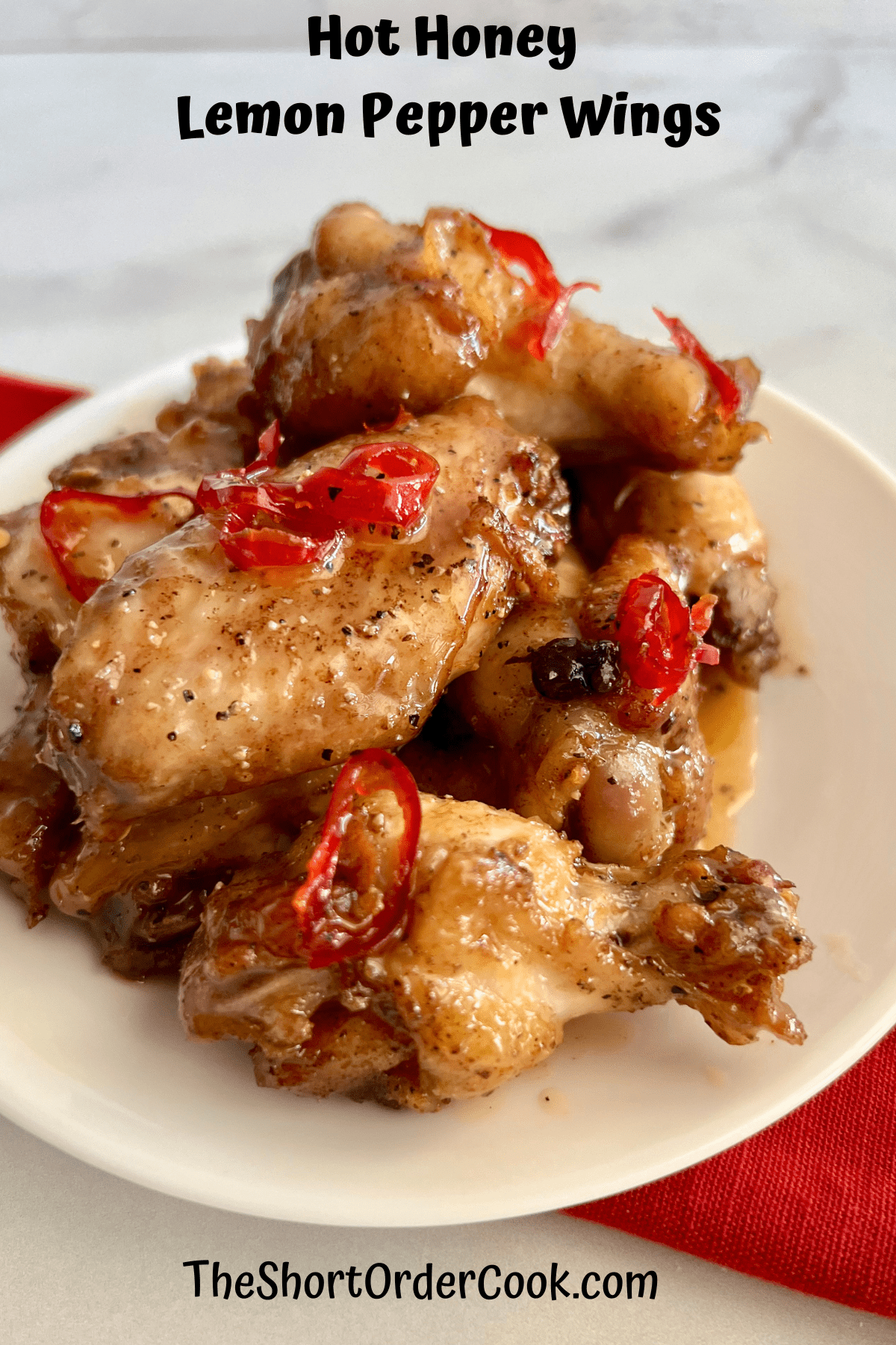 Hot Honey Lemon Pepper Wings piled on a plate with slices of red hot peppers on top.