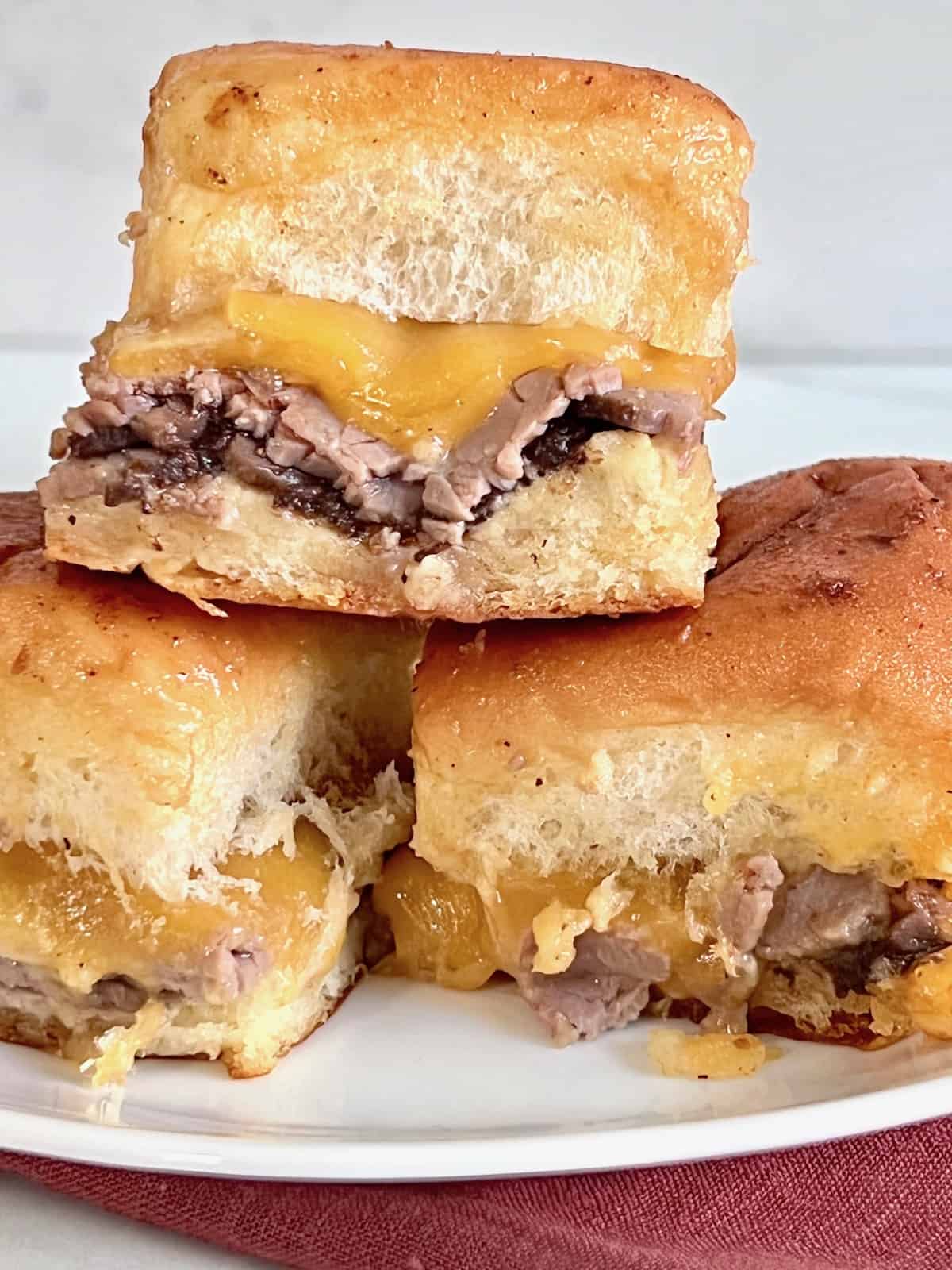Roast Beef, Cheddar, & Caramelized Onion Sliders Closeup stacked on a plate.