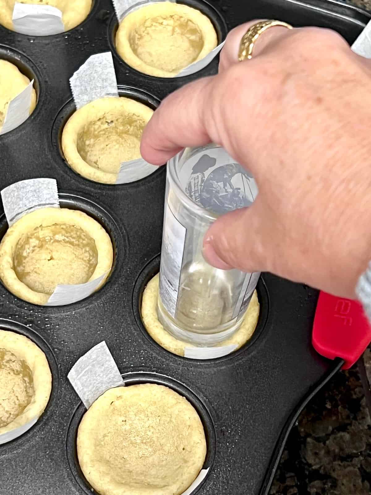 Pressing the hot sugar cookie dough down using a shot glass.