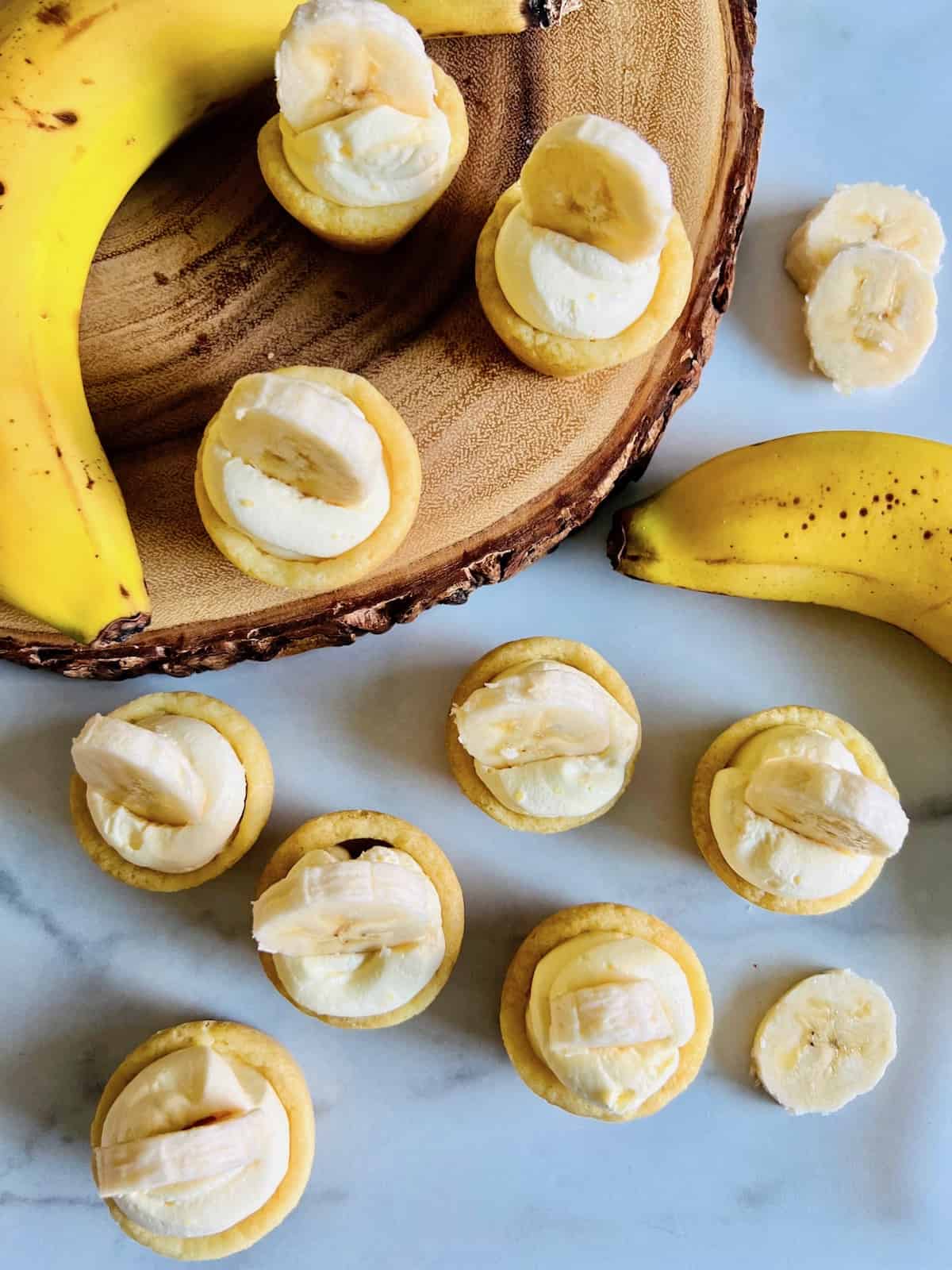 Banana Cream Pie Cookie Cups Topped with banana slices ready to eat on counter and wooden board with bananas next to them.