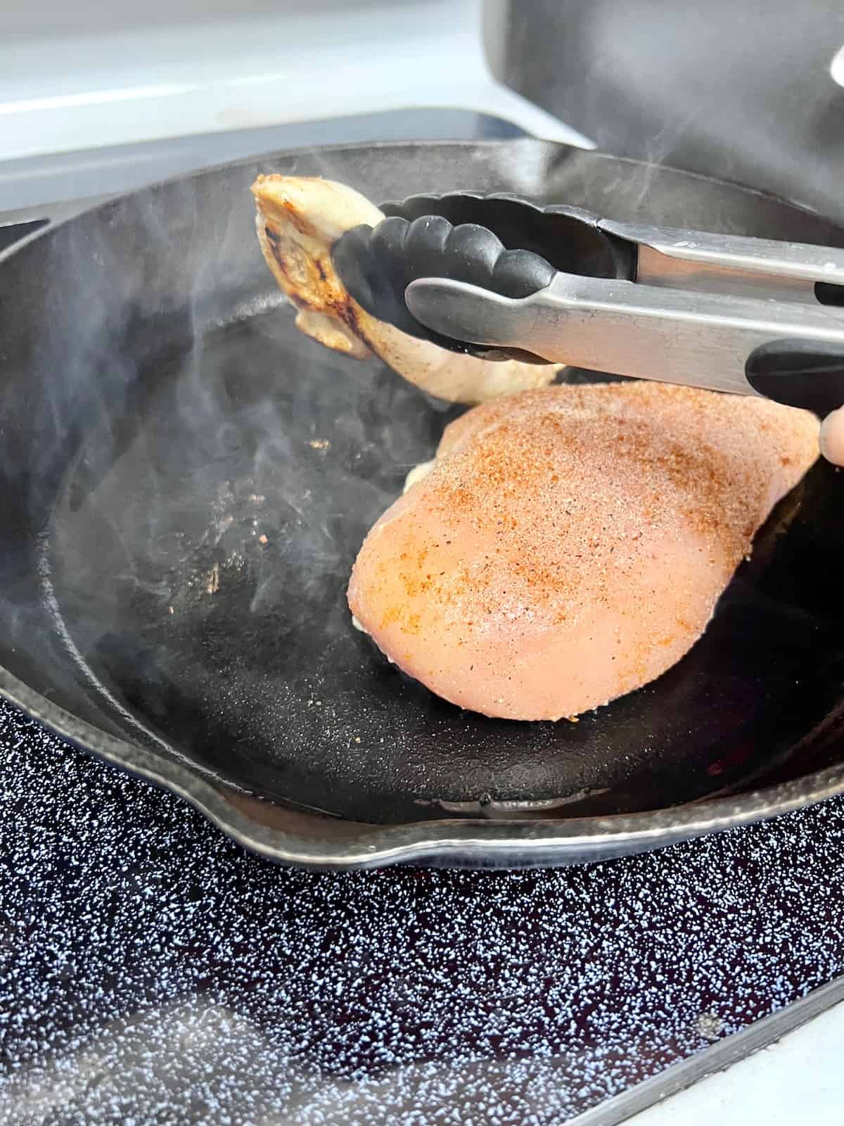 Flipping the chicken to cook the other side in the cast iron skillet.