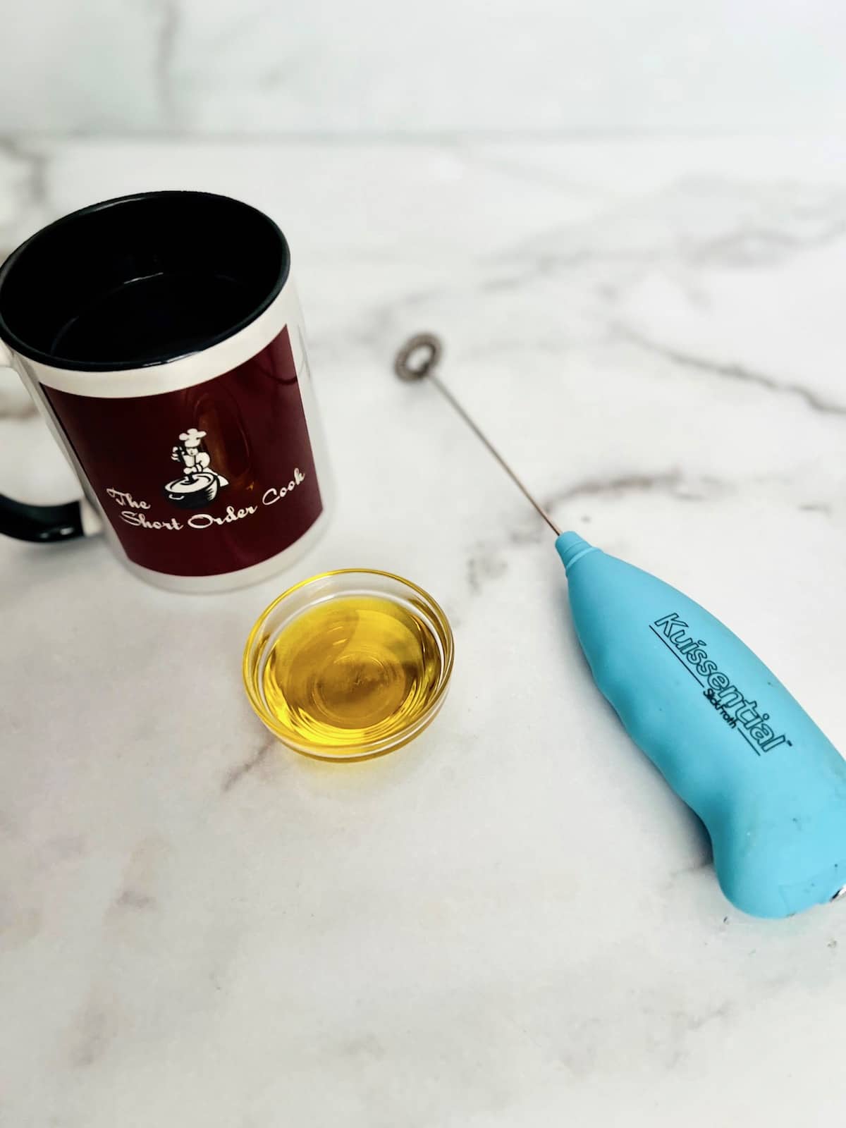 Olive oil and a cup of coffee on the counter alongside a milk frother gadget.