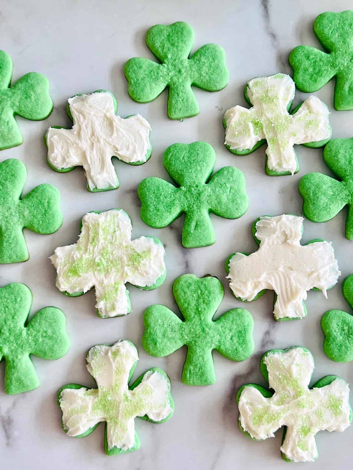 Green Shamrock Sugar Cookies Frosted and some plain cookies ready to eat lined up on a counter