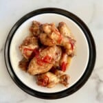 Hot Honey Lemon Pepper wings on a white plate topped with chili peppers.