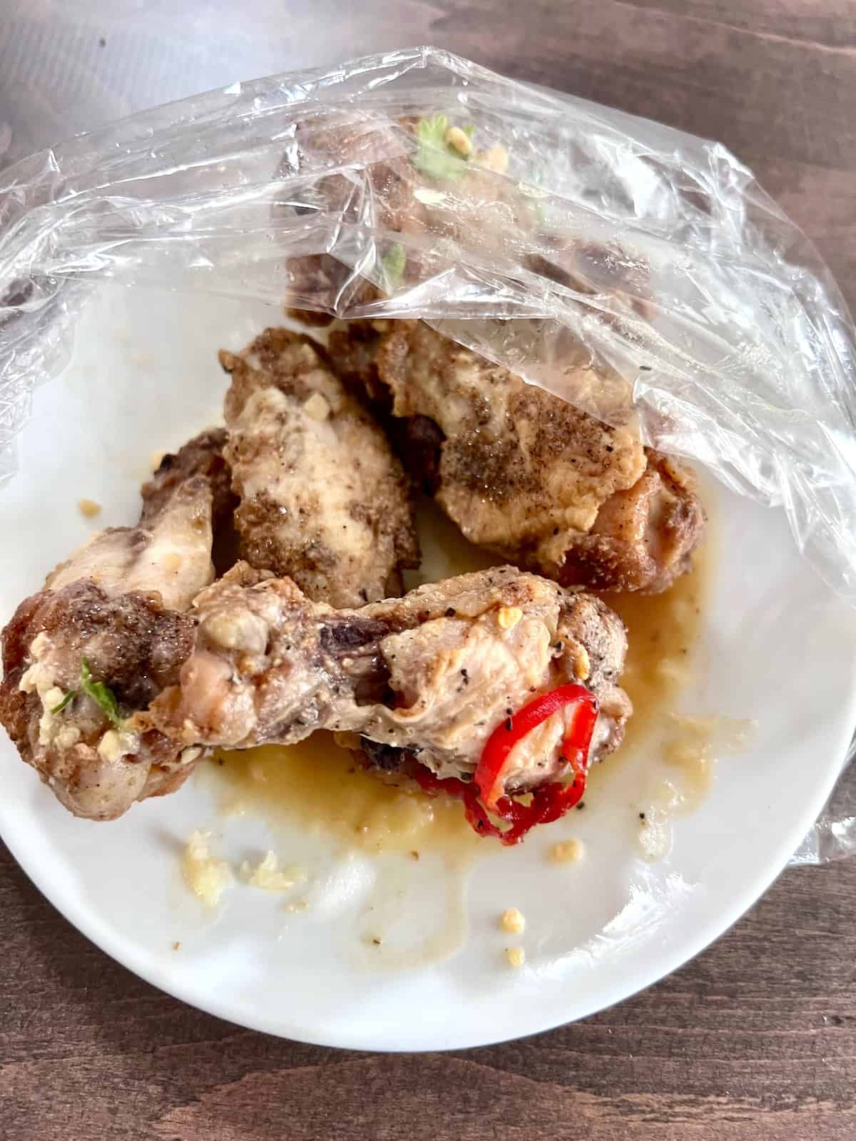 Leftover wings on a plate partially covered in plastic wrap.