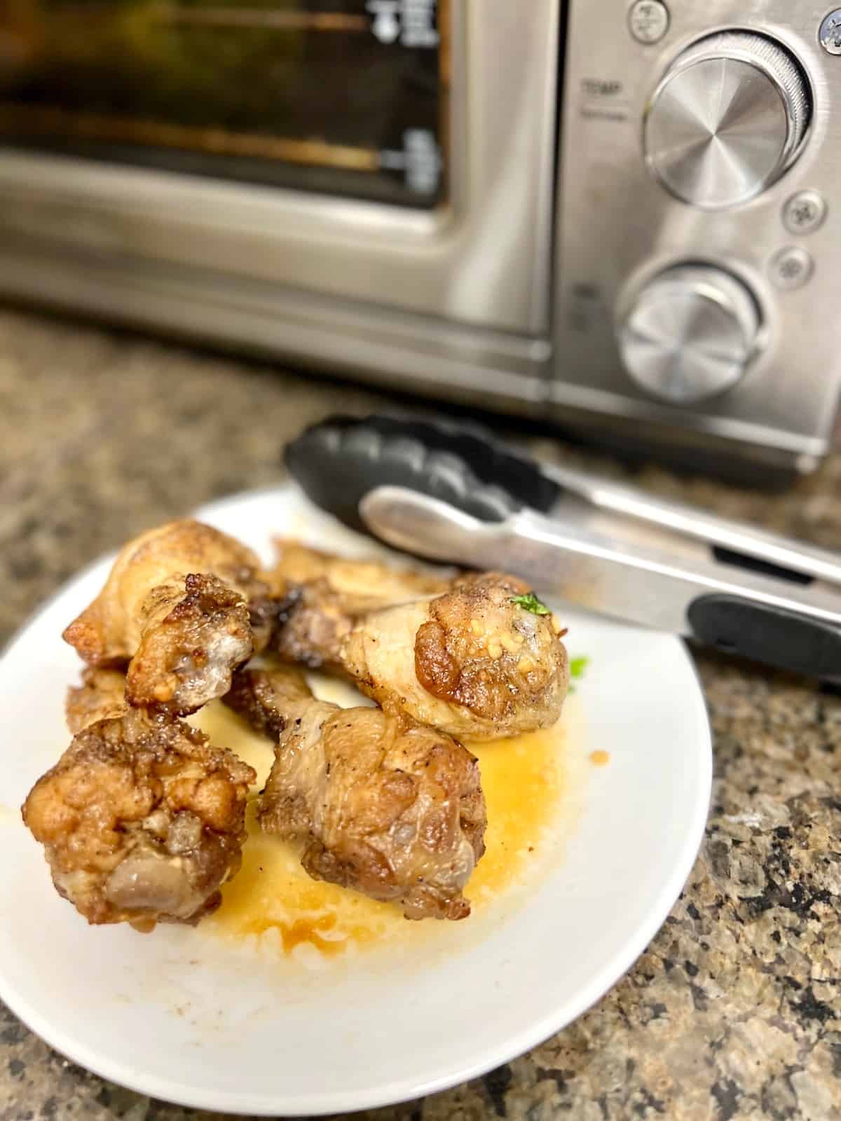 Wings plated in front of air fryer with tongs.