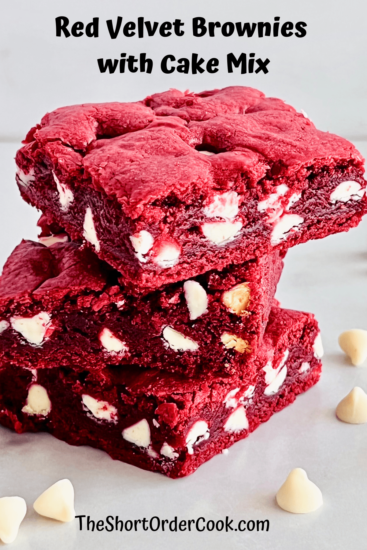 Stacked red velvet brownies with white chocolate chips on a plate.