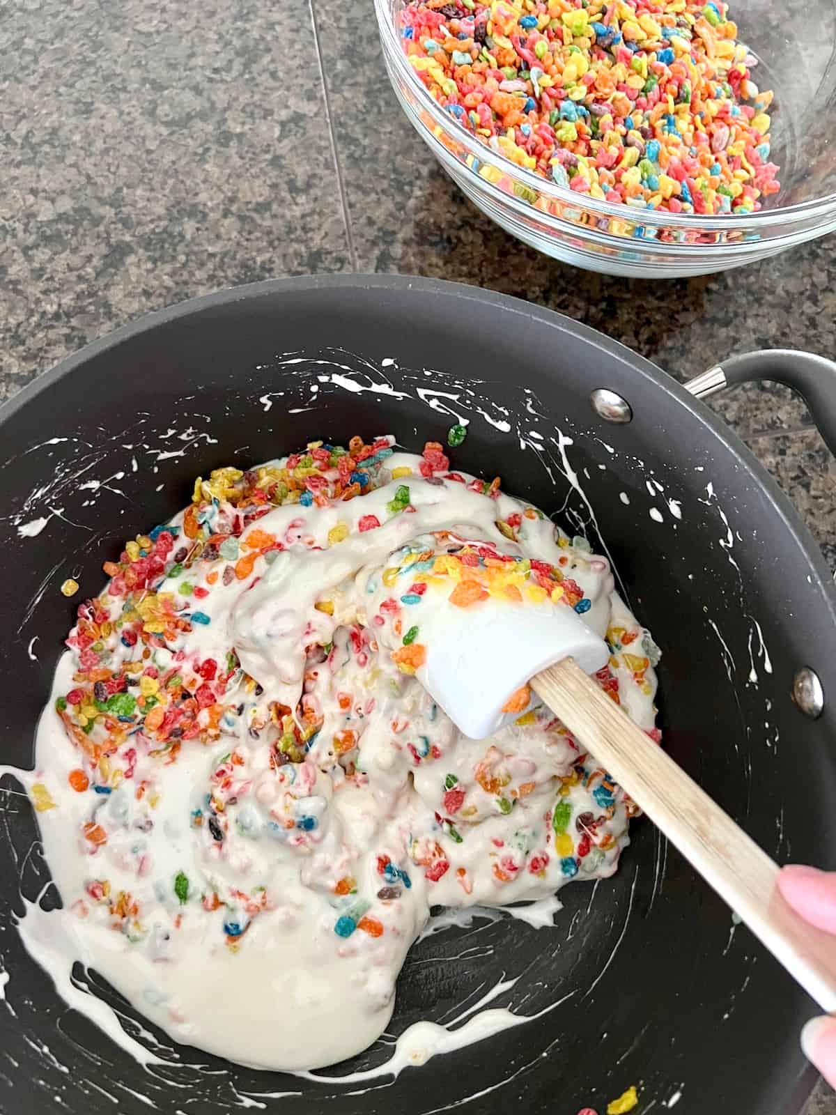 Stirring in the fruity pebbles to the melted marshmallows.