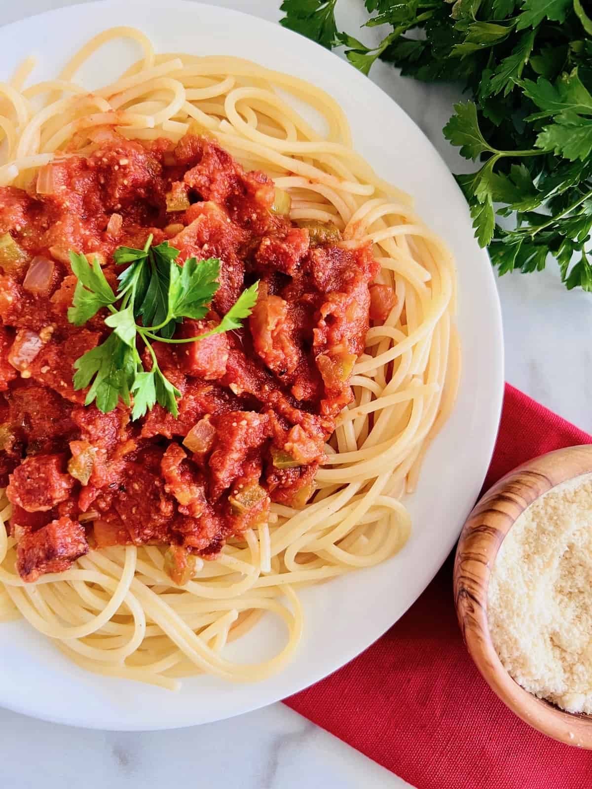 Pepperoni Spaghetti Overhead of plated pasta topped with fresh parsley next to bunch of parsley and bowl of parmesan.