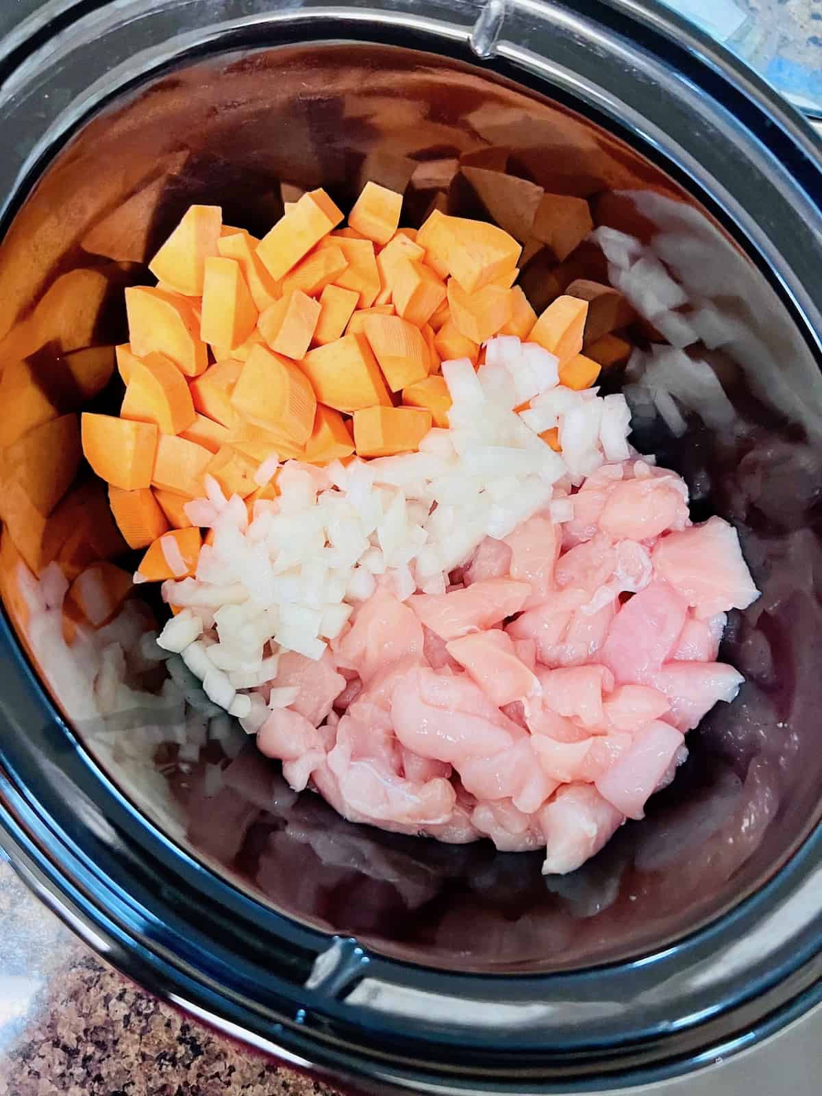 Sweet potatoes onions and diced chicken lined up in crockpot insert.