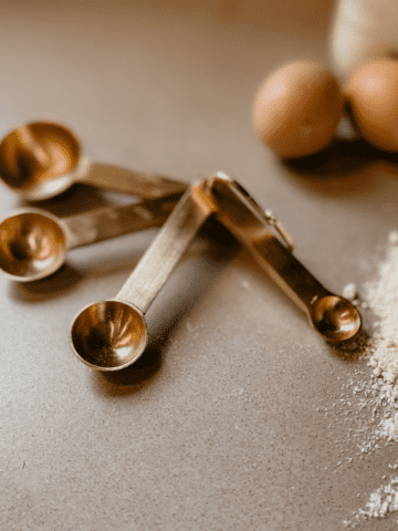 Measuring spoons on a counter with eggs and flour.