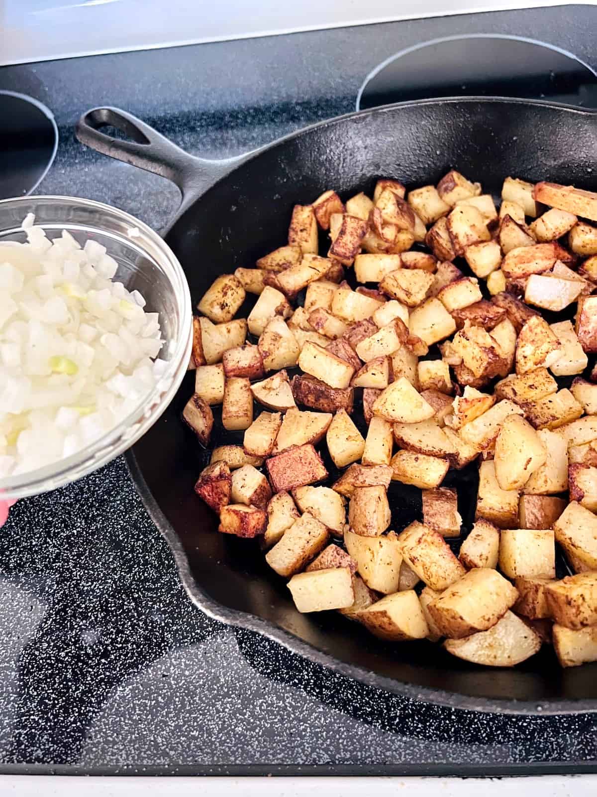 Adding chopped onions to potatoes in the skillet.