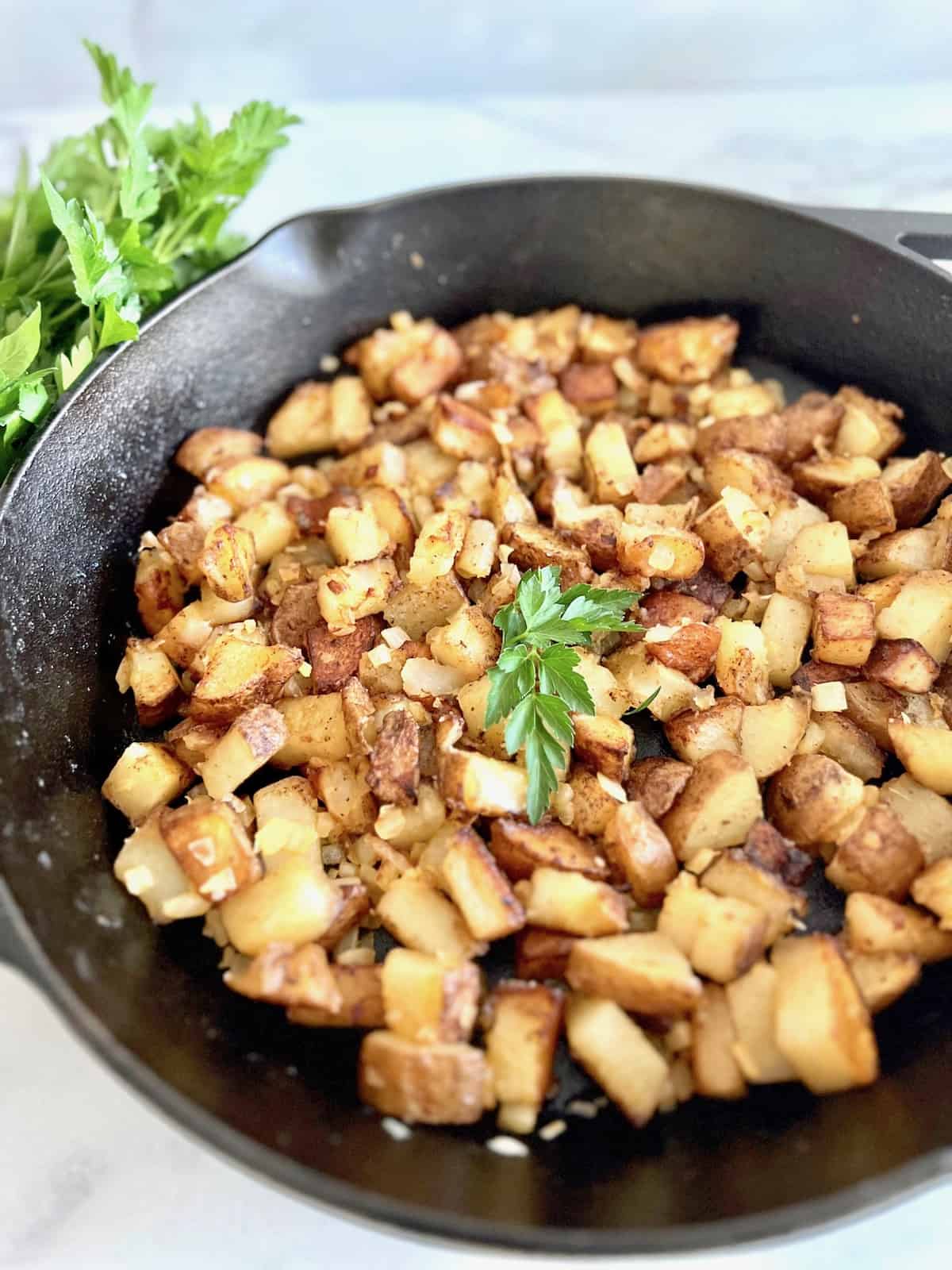 Pan Fried Potatoes & Onions Cast iron skillet filled & topped with parsley.