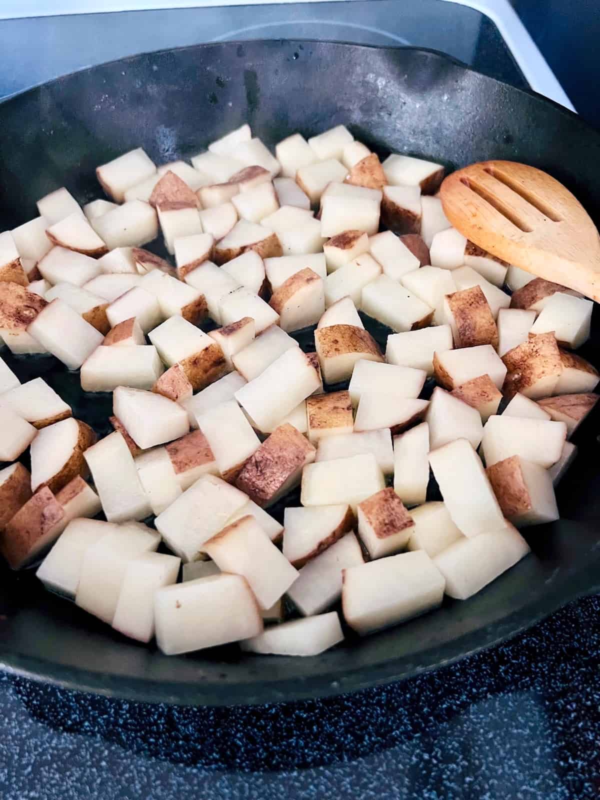 Cubed potatoes in the cast iron skillet with hot oil.