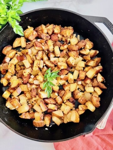 Pan Fried Potatoes & Onions in a cast-iron skillet topped with fresh parsley.
