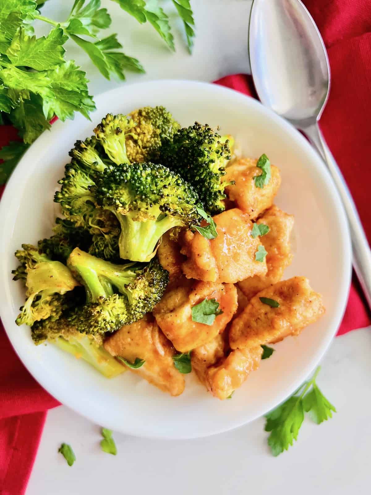 Sheet Pan Buffalo Chicken & Broccoli in a bowl served over rice with spoon red napkin and fresh parsley.