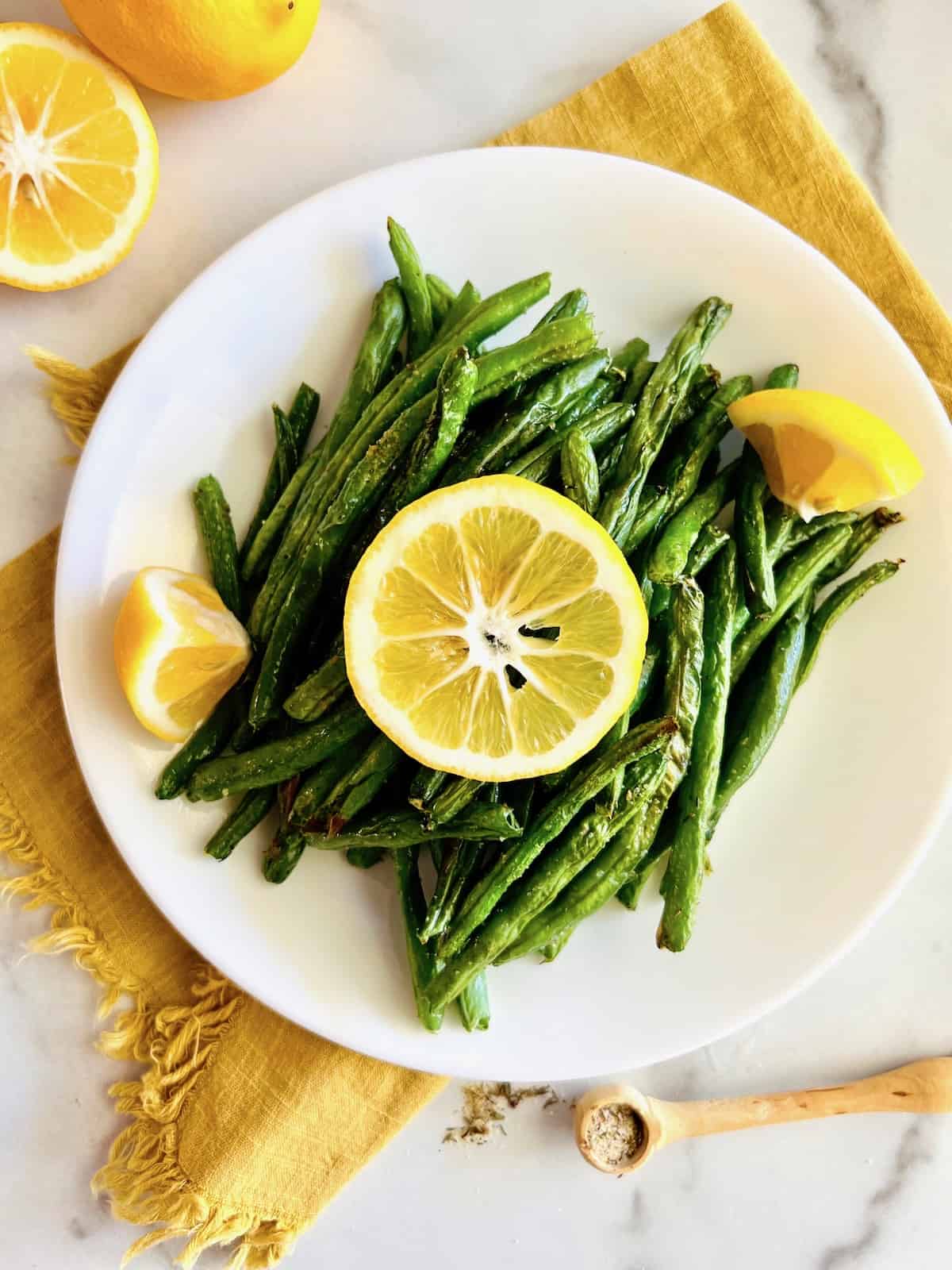 Air Fryer Green Beans Plated and topped with a lemon slice and wedges on the side of the plate.